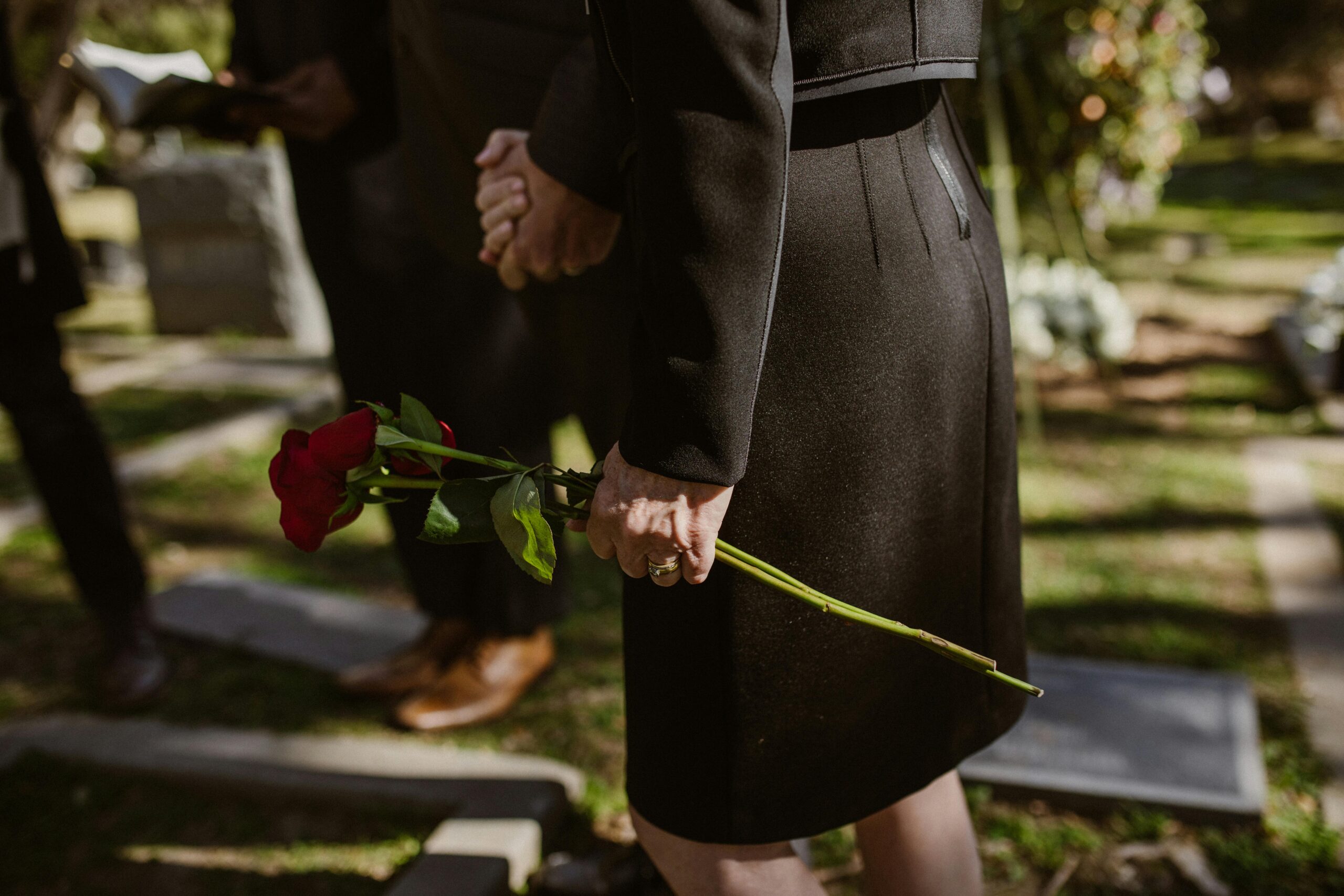 woman in black holding a red rose at a funeral