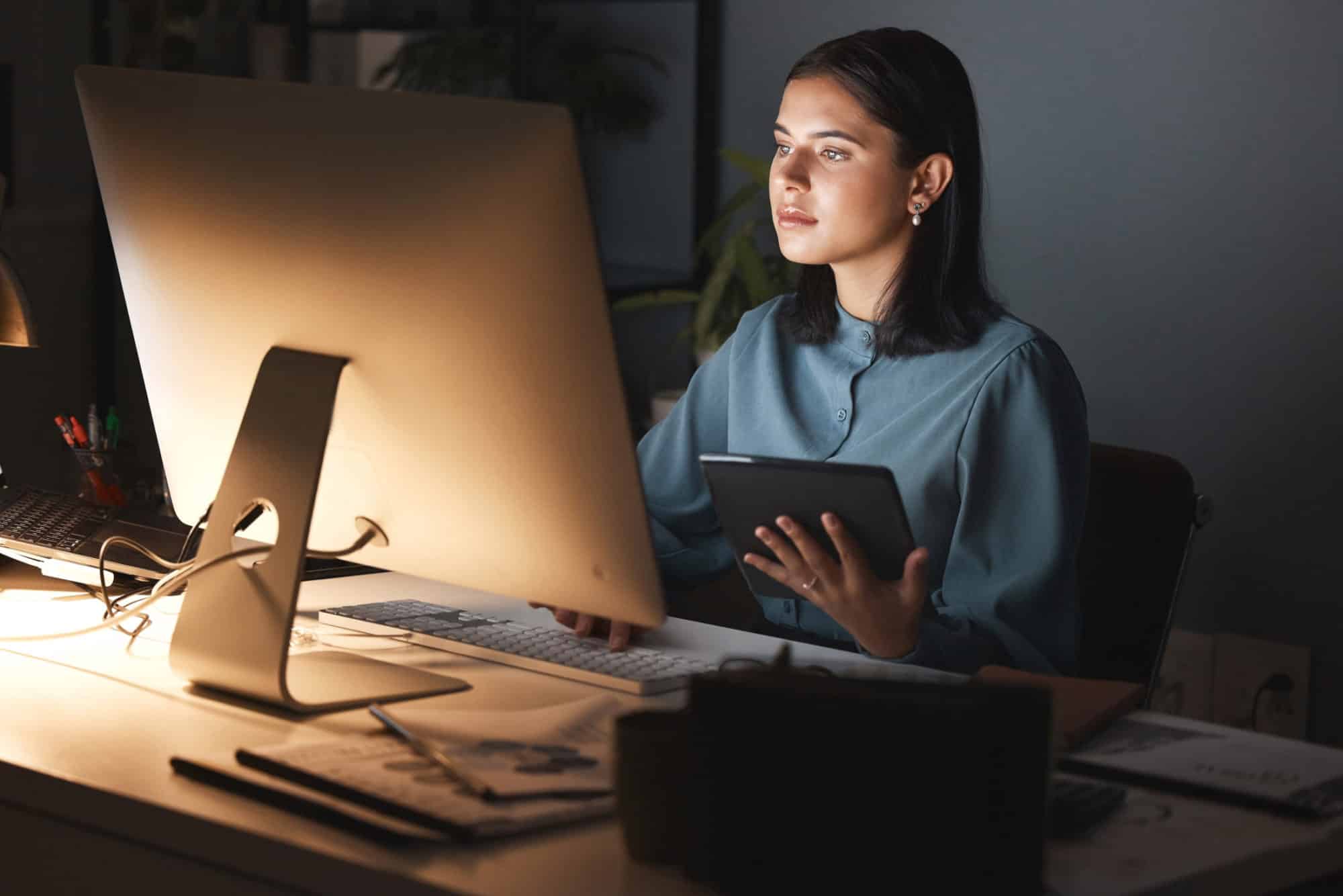 Person working behind a computer holding a tablet