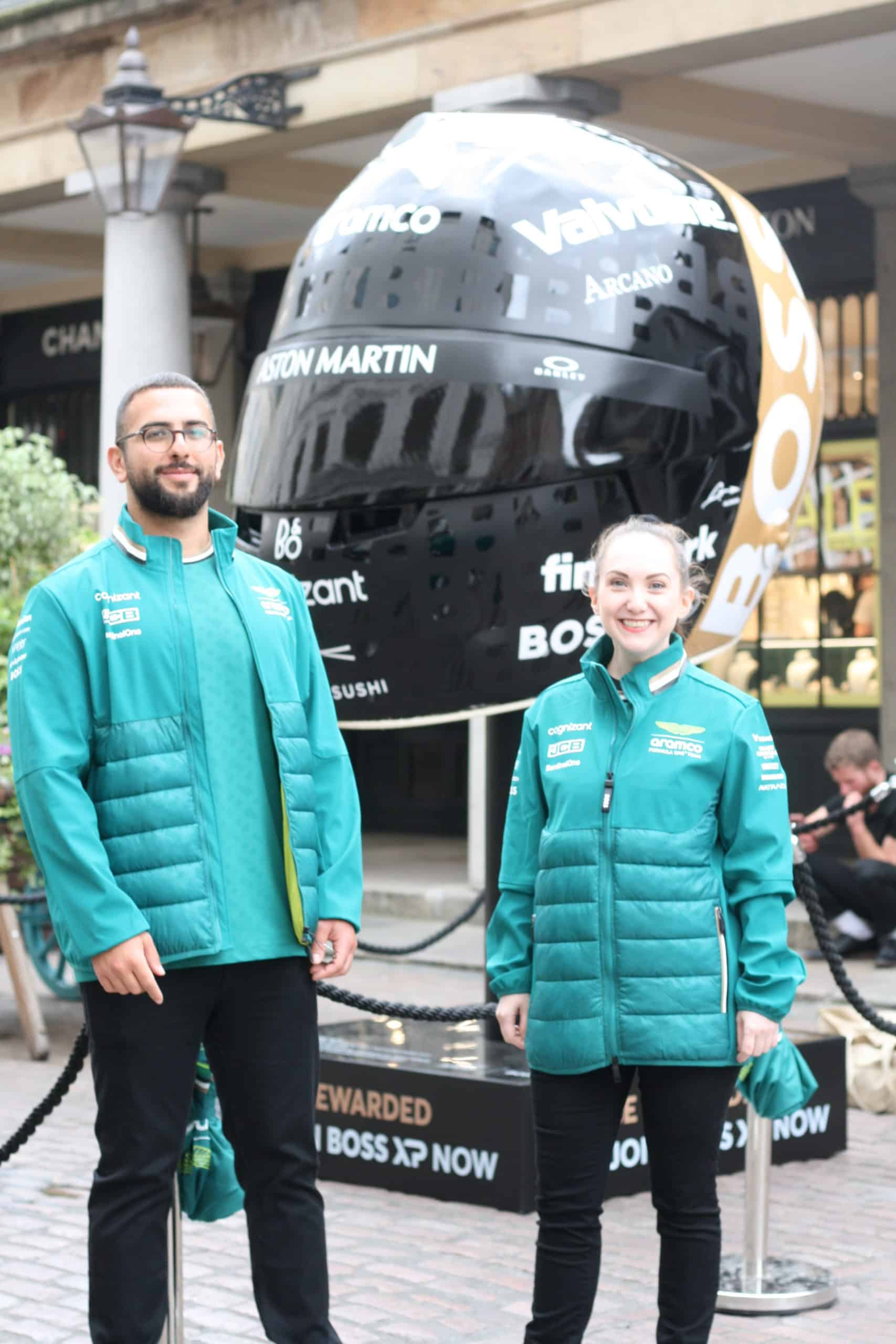 two people standing in front of an oversized f1 helmet