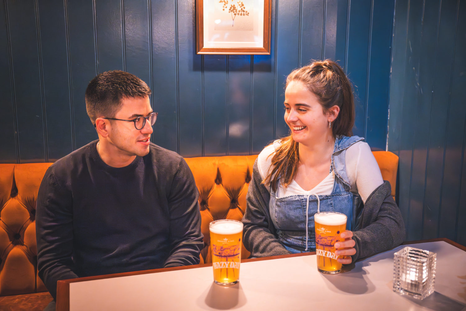 two people looking at each other with beers in front of them